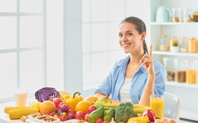 happy young housewife sitting in the kitchen preparing food from a pile of diverse fresh organic fruits and vegetables