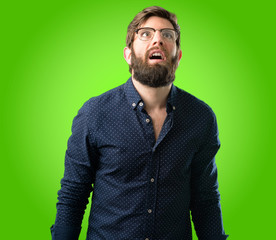Young hipster man with big beard happy and surprised cheering expressing wow gesture over green background
