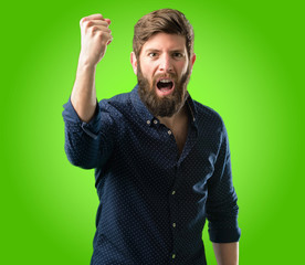 Young hipster man with big beard irritated and angry expressing negative emotion, annoyed with someone over green background