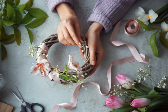 Female decorator creating beautiful wreath at table, top view