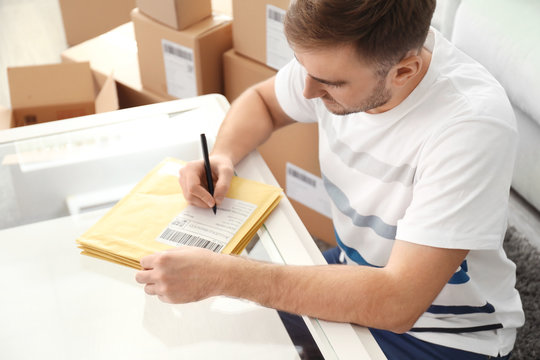 Young man preparing parcel envelopes for shipment to client at home