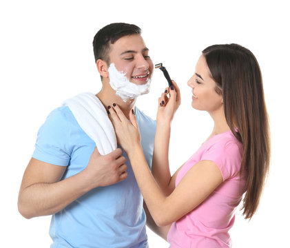 Young woman helping her boyfriend shaving on white background