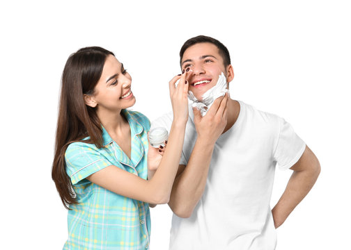 Young man shaving and his girlfriend applying face cream on light background