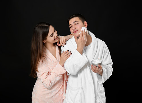 Young man shaving and his girlfriend on dark background