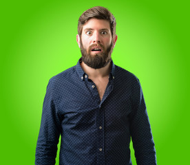 Obraz premium Young hipster man with big beard happy and surprised cheering expressing wow gesture over green background