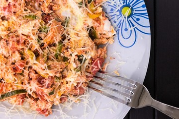 A photo of an omelette with cherry tomatoes, parsley. and grated cheese, shot from above on a rustic wooden texture with a fork and a place for text