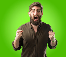Young hipster man with big beard happy and excited celebrating victory expressing big success, power, energy and positive emotions. Celebrates new job joyful over green background