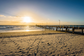 Fototapeta na wymiar Beautiful colorful sunset summer view to the calm great ocean with pure sandy beach and a lovely empty wooden jetty lighten the night at a public boulevard, Glenelg Jetty, Adelaide, South/ Australia