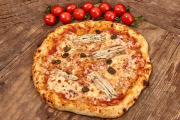 Homemade fresh delicious gourmet pizza Romana whit anchovies,capers and oregano,Tasty italian pizza isolated on wooden table, close up