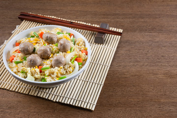 meatball and vegetable fried rice in a ceramic bowl with chopsticks and bamboo mat on wooden table. homemade style healthy food concept.