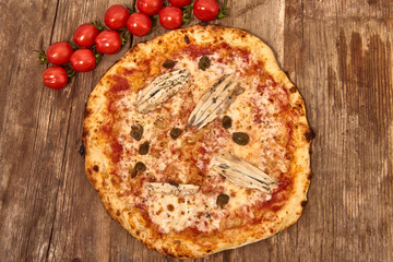 Homemade fresh delicious gourmet pizza Romana whit anchovies,capers and oregano,Tasty italian pizza isolated on wooden table, close up