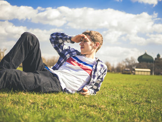 young man protrait on the grass in the park against the blue sky background