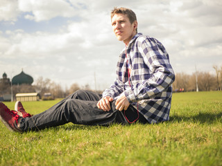 young man listenning to the music in the earbuds during summer sunny day lying on the grass in the park