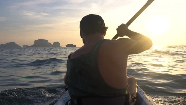 Back View of Strong Man on Kayak in the Open Sea Water. Sunset over the Rock Cliffs. Railey Beach, Krabi, Thailand.