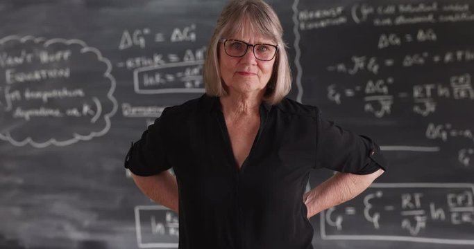 Old senior woman teacher with serious attitude posing in front of chalkboard,  Charming mature woman with arms on her waist looking at camera    , 4k