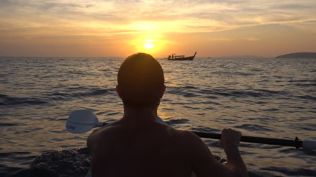 Back View of Strong Man on Kayak in the Open Sea Water. Sunset over the Rock Cliffs. Railey Beach, Krabi, Thailand.