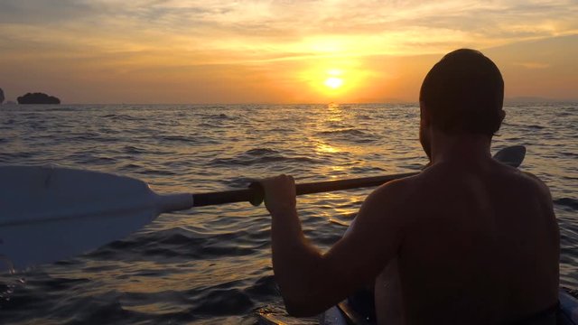 Back View of Strong Man on Kayak in the Open Sea Water. Sunset over the Rock Cliffs. Railey Beach, Krabi, Thailand.