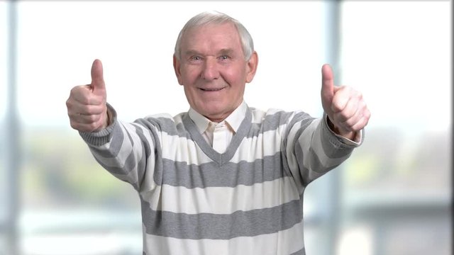 Beautiful old man with two tumbs up. Cheerful caucasian senior showing two thumbs up on blurred background.