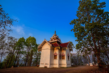 Fototapeta premium Golden light shining on white and gold pagoda during sunrise / sunset with blue sky in Mae hong son Thailand