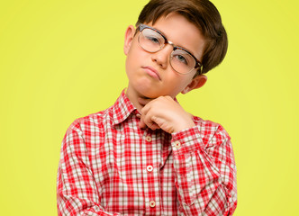Handsome toddler child with green eyes thinking thoughtful with smart face, expressing question and doubt. Imagine the solution over yellow background