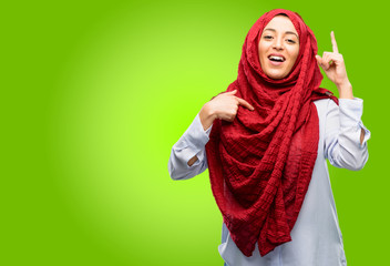 Young arab woman wearing hijab happy and surprised cheering expressing wow gesture pointing up