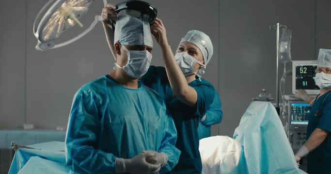 Nurse assisting surgeon with mounting augmented reality holographic hololens glasses before operation. 4K UHD 60 FPS SLO MO