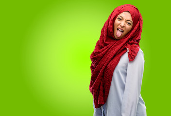 Young arab woman wearing hijab sticking out tongue at camera at sign of disobedience, protest and...