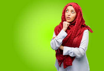 Young arab woman wearing hijab thinking and looking up expressing doubt and wonder