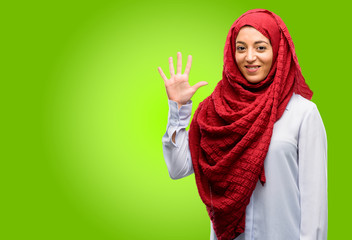 Young arab woman wearing hijab raising his finger, is the number five