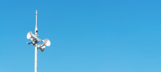 Outdoor loudspeaker alert system against a blue sky