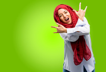 Young arab woman wearing hijab making rock symbol with hands, shouting and celebrating