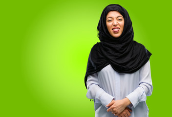 Young arab woman wearing hijab sticking out tongue at camera at sign of disobedience, protest and...