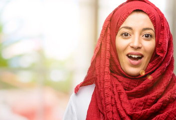 Young arab woman wearing hijab happy and surprised cheering expressing wow gesture