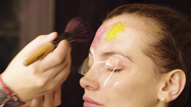 Close up. Face art. The make-up artist begining to paint on the face of the model. Application of glitter powder