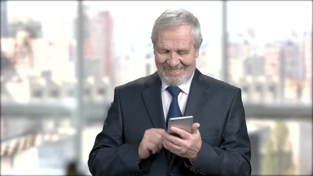 Senior financial manager texting a message. Elderly businessman answering the smartphone, send a mail and smiles for the beautiful job news. Business, office work and people.