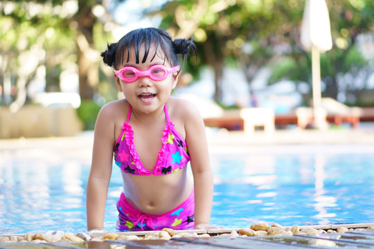 Asian children cute or kid girl wear pink bikini and goggles for swimming and smile with happy fun on swimming pool or water park and nature for refreshing and relax with exercise on summer holiday