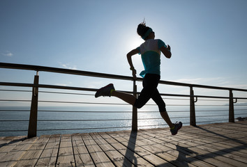 Sporty fitness female runner running on seaside boardwalk during sunrise
