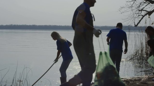 Man and woman in t-shirts of volunteer community taking care of forest ecology cleaning up trash on pond.