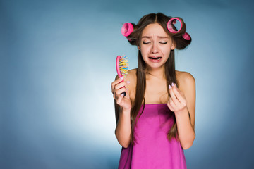 sad young girl loses her hair, holds a comb and cries, on her hair curlers head