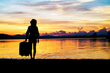 woman traveler have baggage and guitar standing and looking for view of lake mountain and sunset near the dam on vacation.silhouette concept. 