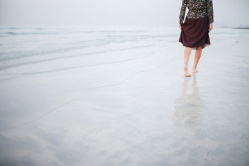 A beautiful girl is walking along the shore against a beautiful sunset