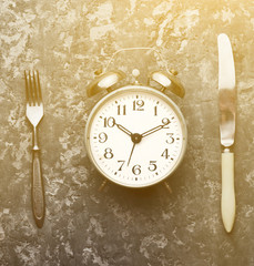 Time for breakfast. Alarm clock, fork and knife on a concrete table. Top view. Flat lay.