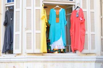 Women's stylish oriental style ethnic dresses in store at display window, in summer street market. Modern fashion shop / Textile souk (bazaar) with colorful tunics in window.