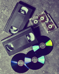 Entertainment and media technology from the 90s. CD's, audio cassettes, video cassettes on a black...
