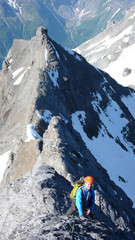 male mountain climber on his way to a high alpine summit on a steep and exposed rock ridge on a...