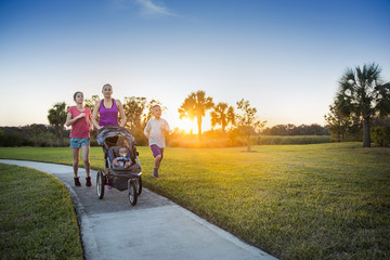 Beautiful, fit young family walking and jogging together outdoors along a paved sidewalk in a park...
