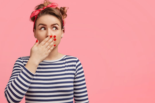 Frightened female in shock, has red manicure, nice make up, wears striped clothing, looks with scared expression upwards, isolated over pink background with blank copy space for your advertisment