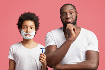 Fatherhood, skin care and hygiene concept. Handsome male teenager learns to shave, has shaving gel...
