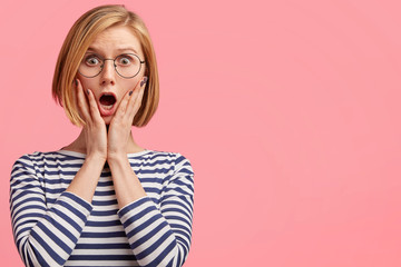 Adorable young stunned woman has bobbed hairstyle, looks in stupor with bated breath at camera, keeps mouth opened, isolated over pink background with balnk copy space for your promotional text