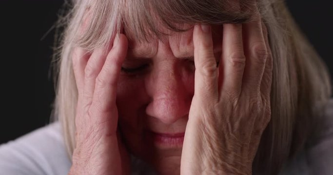 Close up of stressed senior woman face in pain on gray background, Tight shot of elderly woman with migraine headache rubbing head on gray backdrop, 4k 